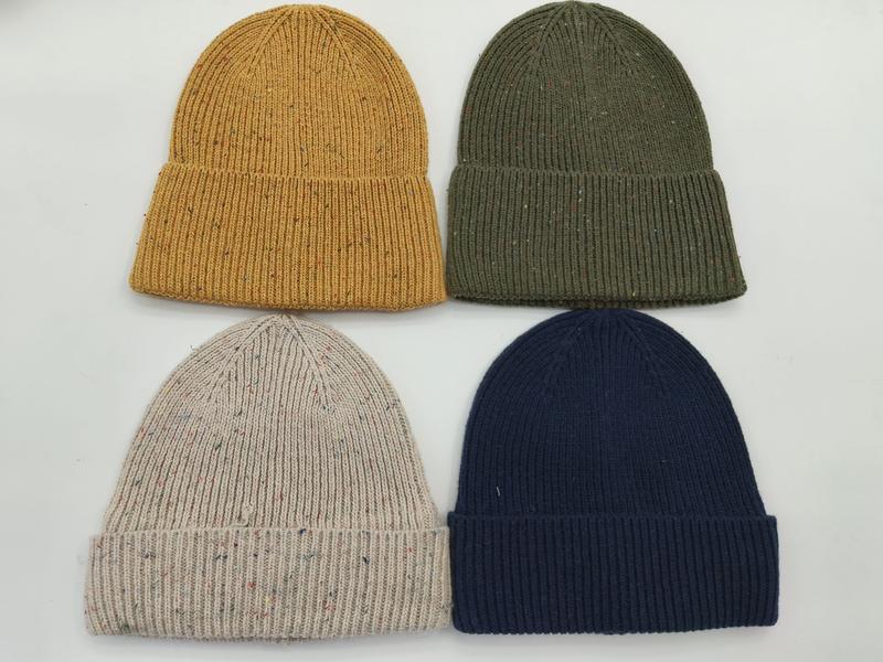 Four ribbed knit beanies in mustard yellow, olive green, oatmeal fleck, and navy blue laid flat on white background