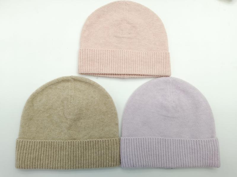 Three knit beanie hats laid flat in blush pink, taupe beige, and lavender with ribbed cuffs on white background