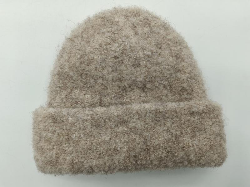 Oatmeal beige boucle knit cuffed beanie hat with fluffy textured yarn, laid flat on white background
