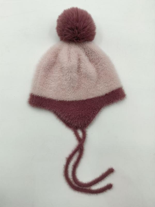 Dusty pink fuzzy knit earflap winter beanie hat with dark mauve pom-pom and tie strings laid flat