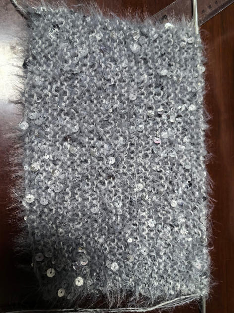 Close-up of grey fluffy knitted fabric swatch with scattered silver sequins on wooden surface