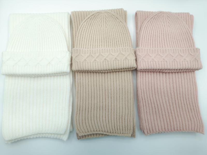 Three matching cable knit beanie hat and ribbed scarf sets in ivory, taupe, and blush pink arranged side by side on white background
