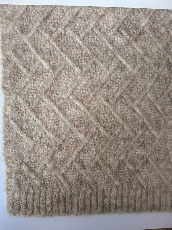 Close-up of a beige diamond lattice knit wool blend throw blanket with ribbed border edge