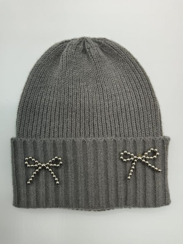 Grey ribbed knit winter beanie hat with two silver beaded bow brooches on folded cuff, flat lay on white background