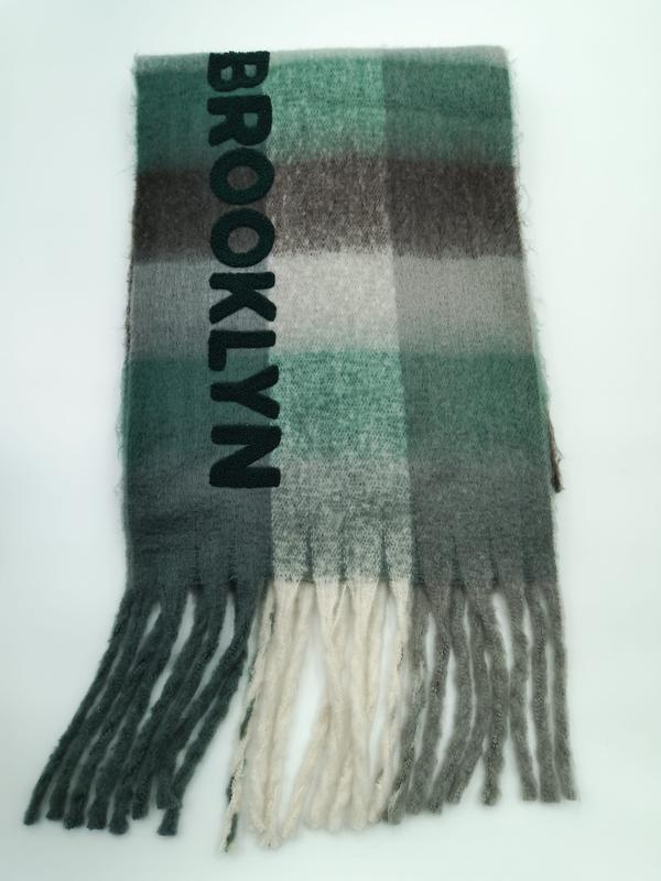Folded green grey and cream plaid scarf with Brooklyn embroidered lettering and fringe tassels on white background