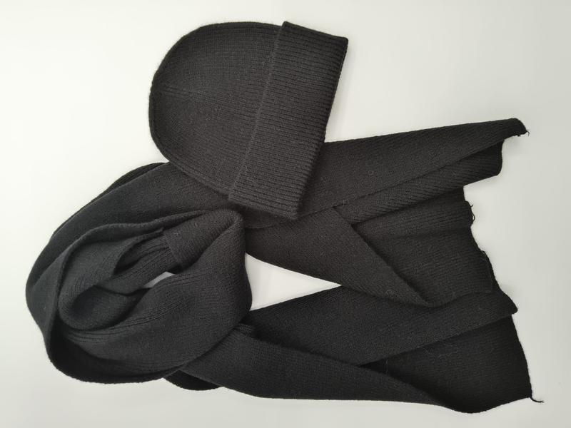 Black ribbed knit beanie hat paired with a long knitted scarf, laid flat on white background showing texture