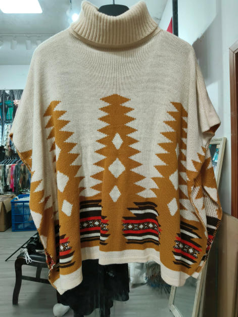 Oversized cream knit poncho sweater with mustard and red Aztec geometric pattern and turtleneck collar on hanger