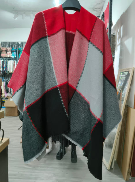 Oversized woven poncho cape with red, grey, and black geometric color block pattern displayed on hanger in store
