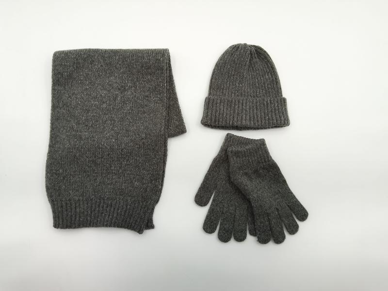 Flat lay of a matching grey marl knitted winter accessories set including a folded scarf, ribbed beanie hat, and gloves on white background