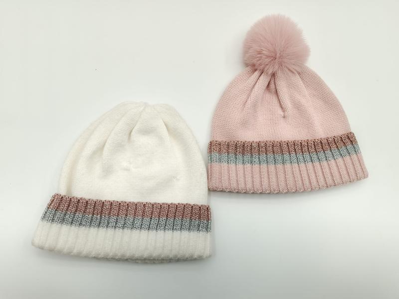 Two knit beanies in white and pink with rose gold and silver metallic stripe cuffs, pink hat has fur pom-pom on top