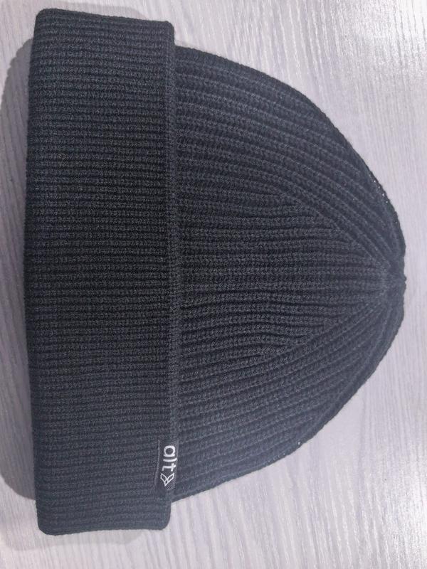 Black ribbed knit cuffed beanie hat laid flat on a light surface, showing textured knit pattern and folded brim