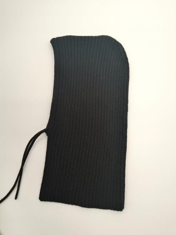 Black ribbed knit balaclava ski mask laid flat on white surface showing curved hood opening and drawstring tie detail