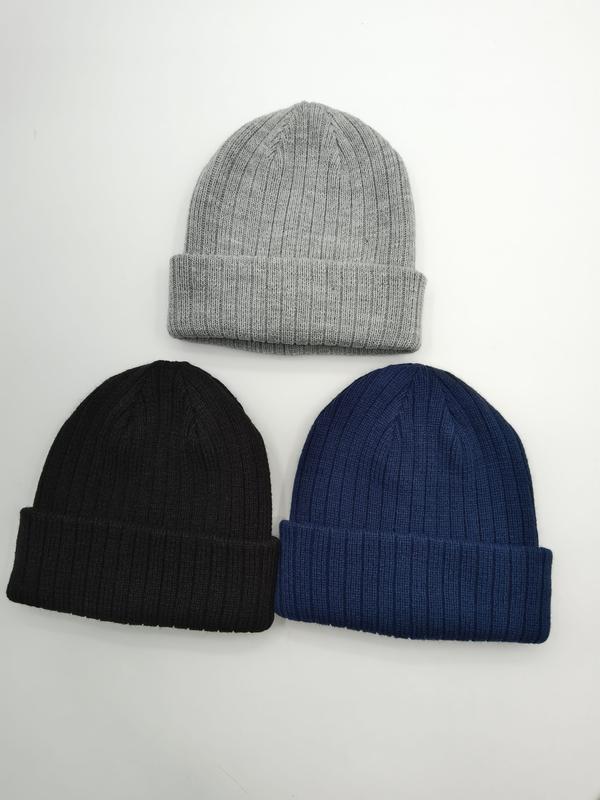 Three ribbed knit cuffed beanie hats laid flat in light grey, black, and navy blue on white background