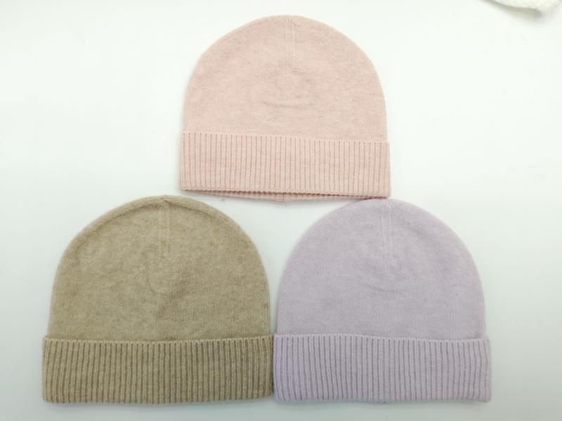 Three knit beanie hats laid flat in blush pink, taupe beige, and lavender with ribbed cuffs on white background